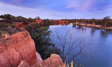 Red cliffs of Murray river on the border between Victoria and New South Wales states of Australia. Elevated red bank of the river overlooks river bend with cruise ship at sunset.